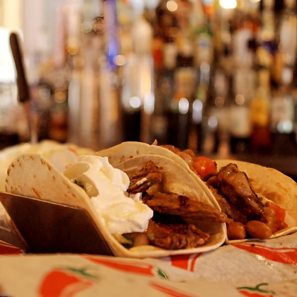 Close-up of two El Patron Mexican Restaurant tacos with meat, beans, and sour cream, bar in background.